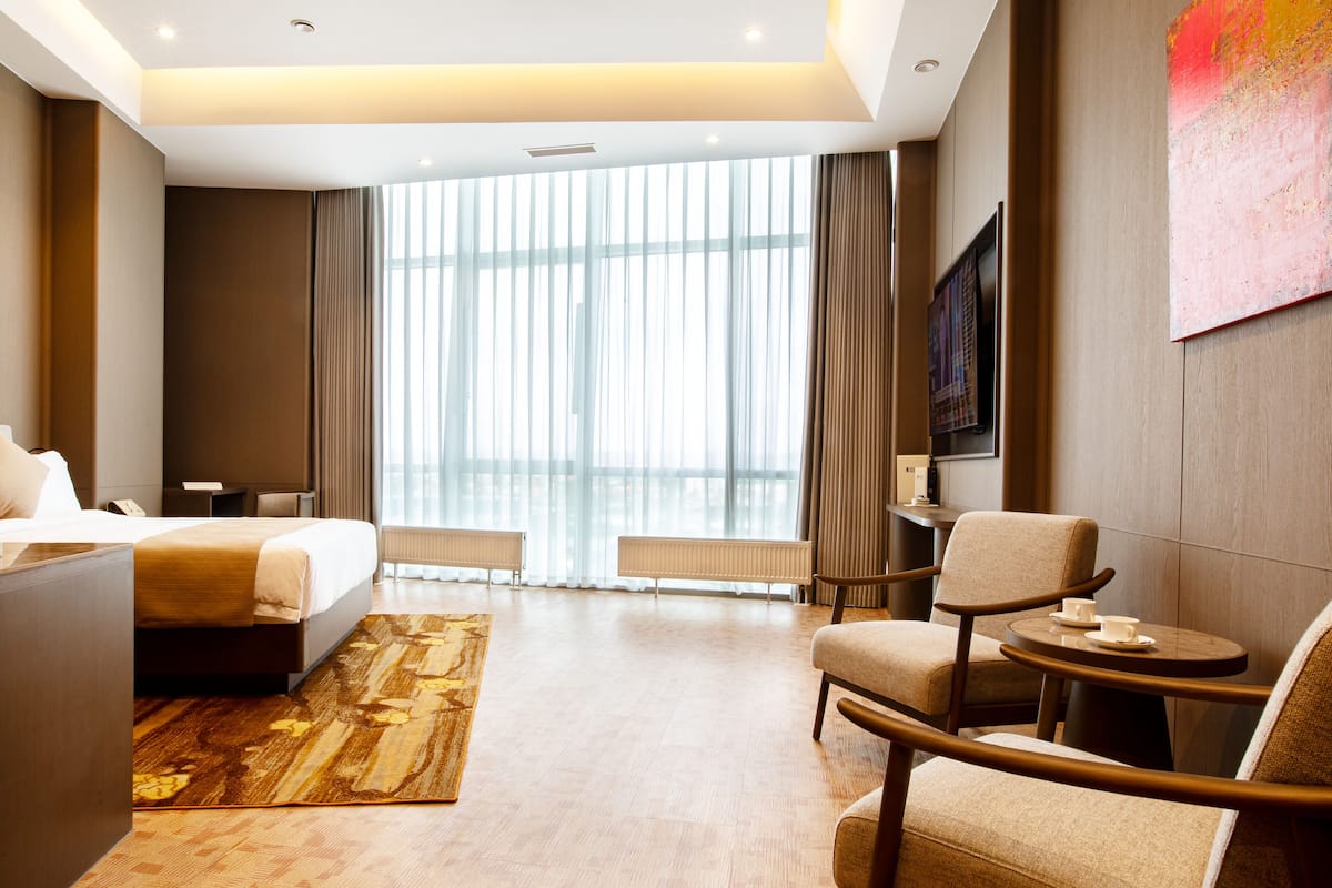 A hotel room with a bed, a sofa, a small table, and a large window with curtains.