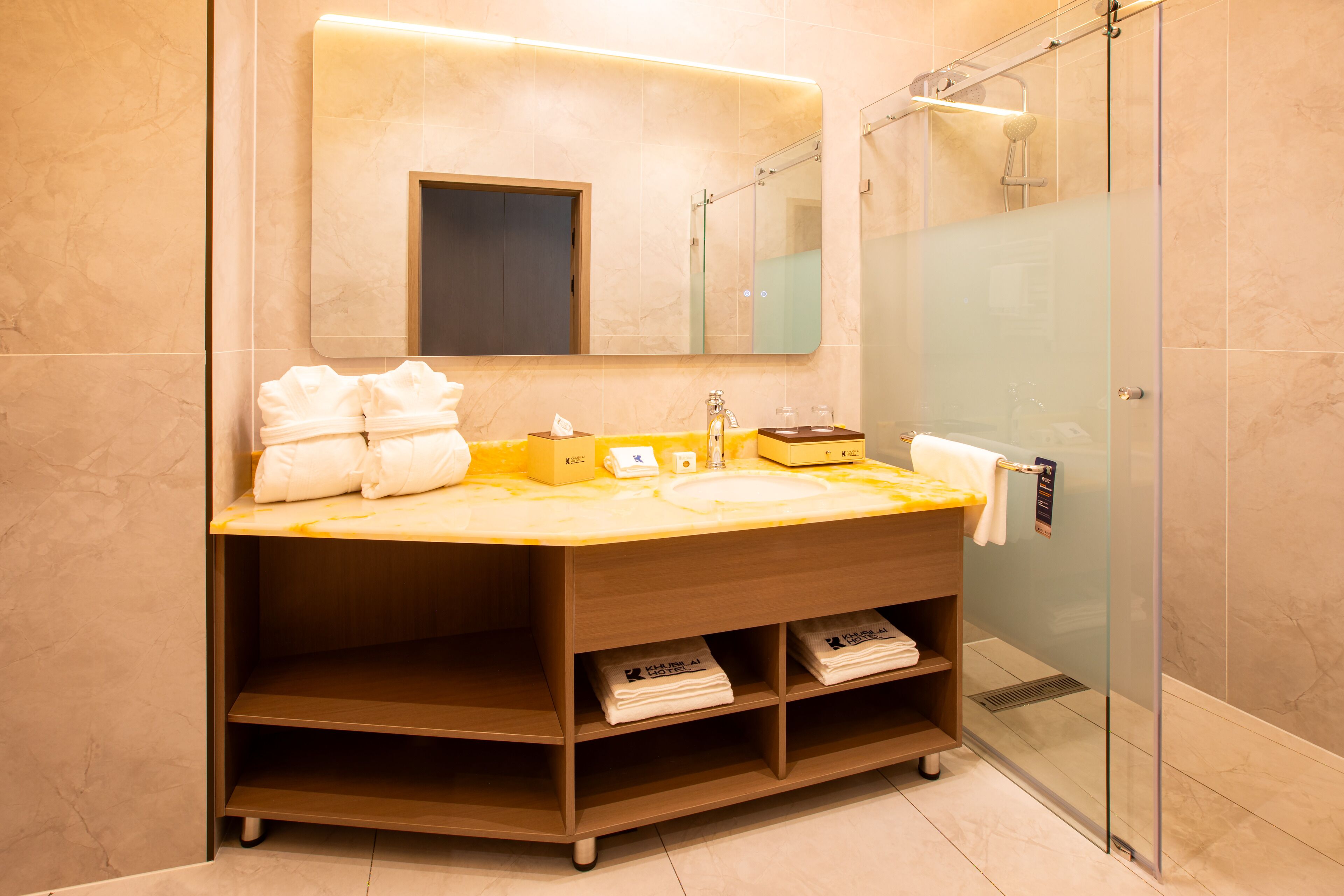 Un baño moderno con un espejo grande, un lavamanos, cabina de ducha con paredes de vidrio y un mueble de tocador de madera con estantes.