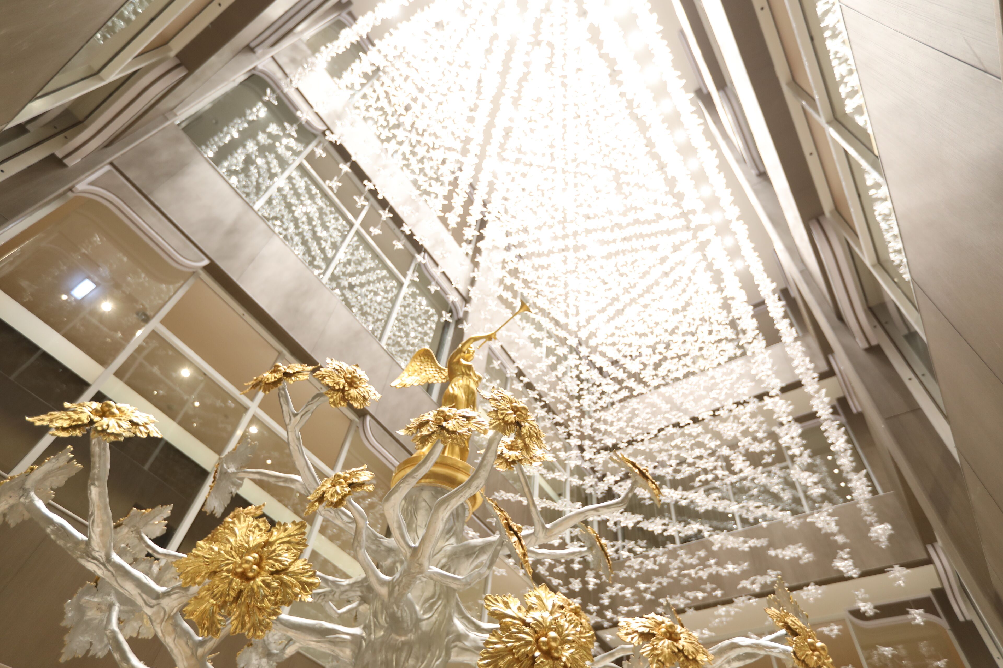 A chandelier with golden and silver elements, a ceiling with a geometric pattern, and a reflective floor.