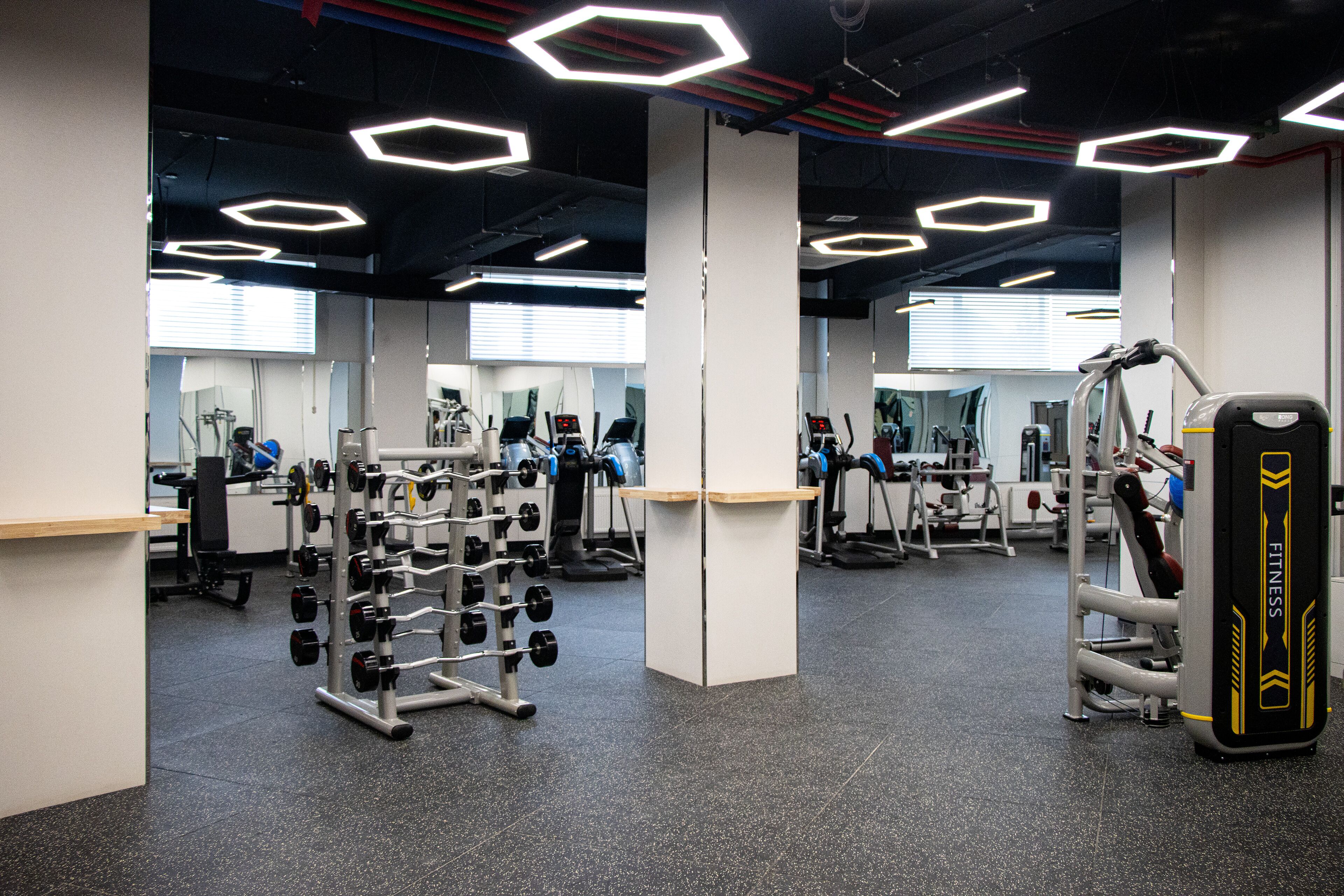 Un gimnasio con equipo de ejercicio, espejos e iluminación de techo hexagonal.