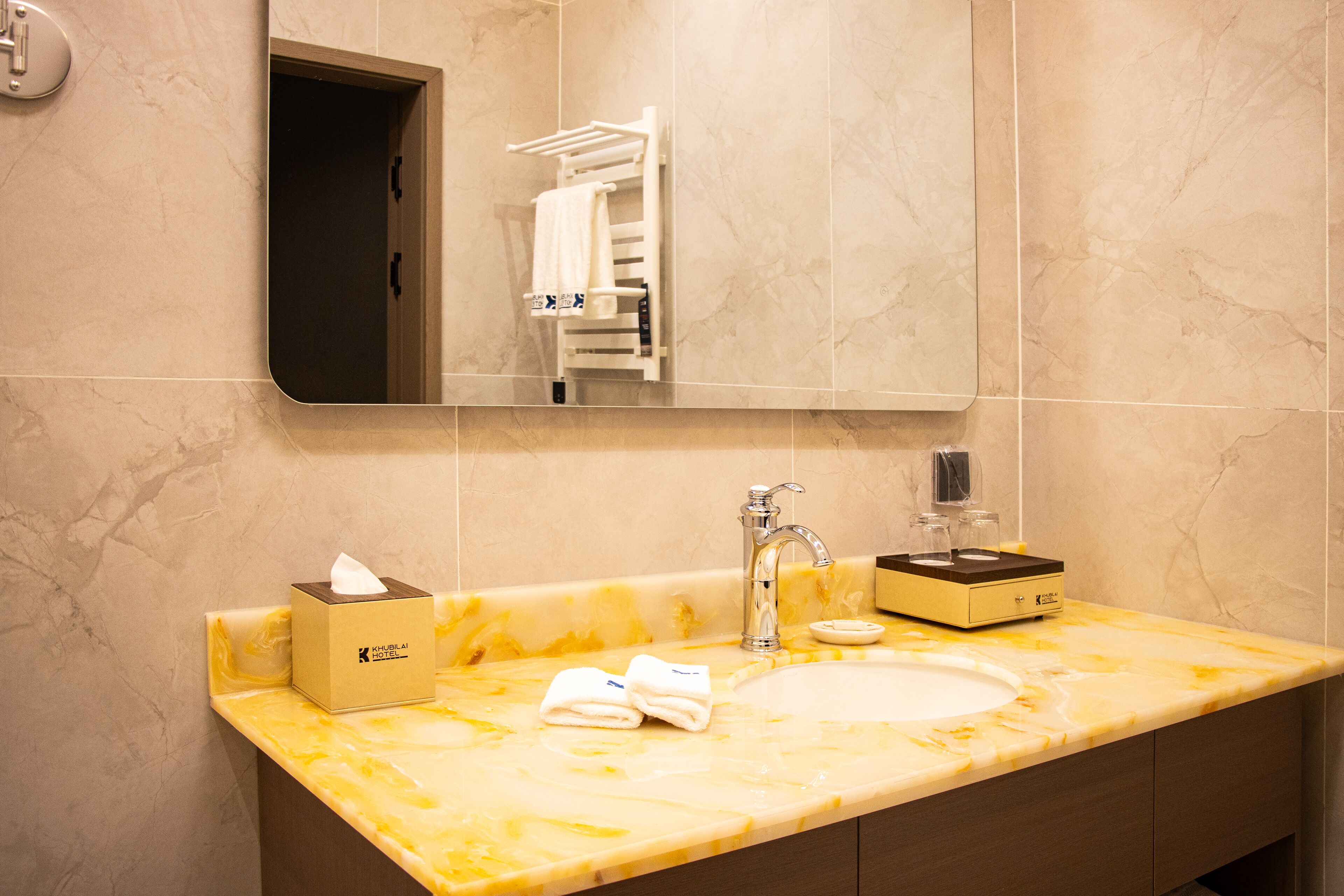 A bathroom with a marble sink, a towel rack, a mirror, and a tissue box.
