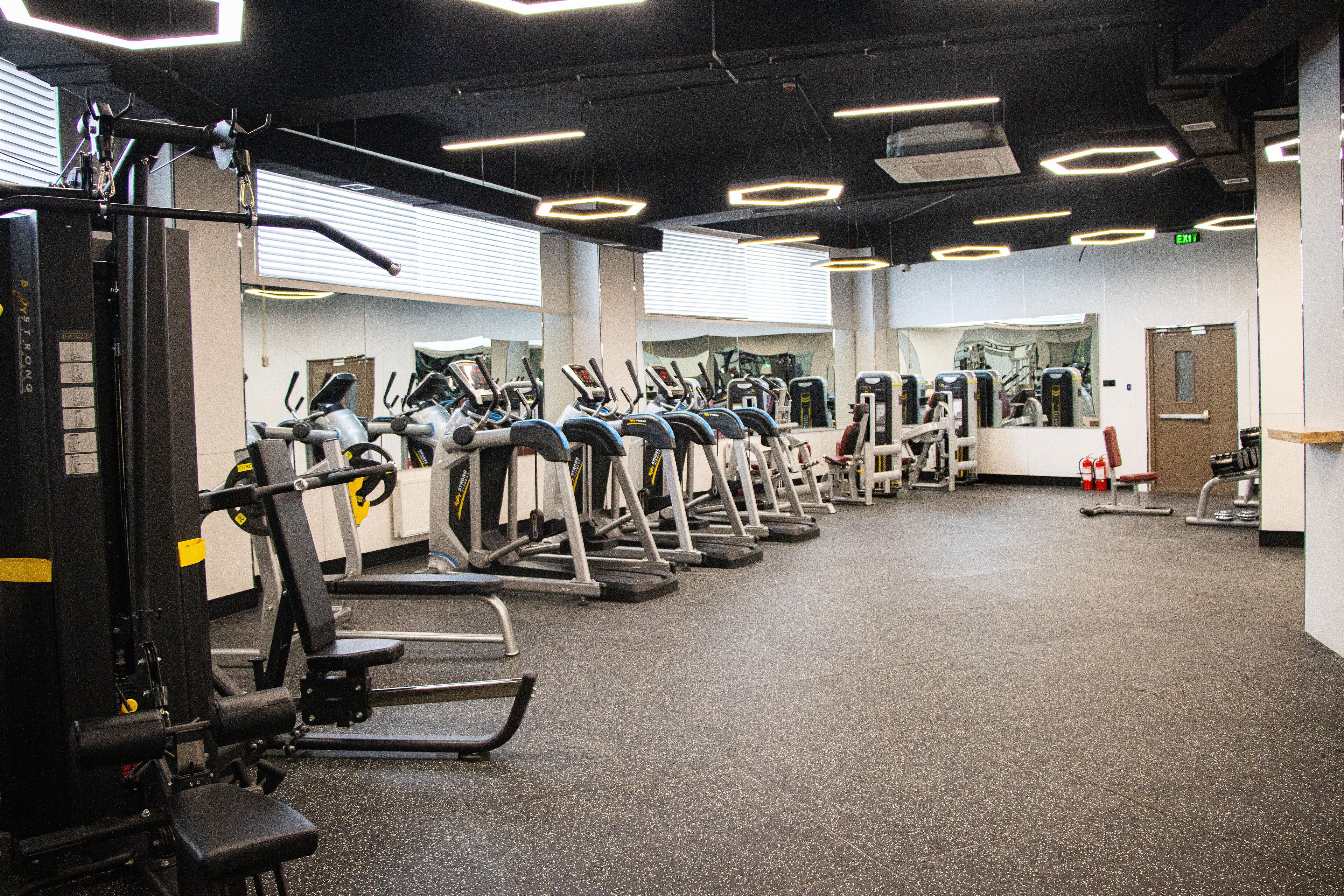 A gym with multiple exercise machines, a mirrored wall, and a clean, modern design.