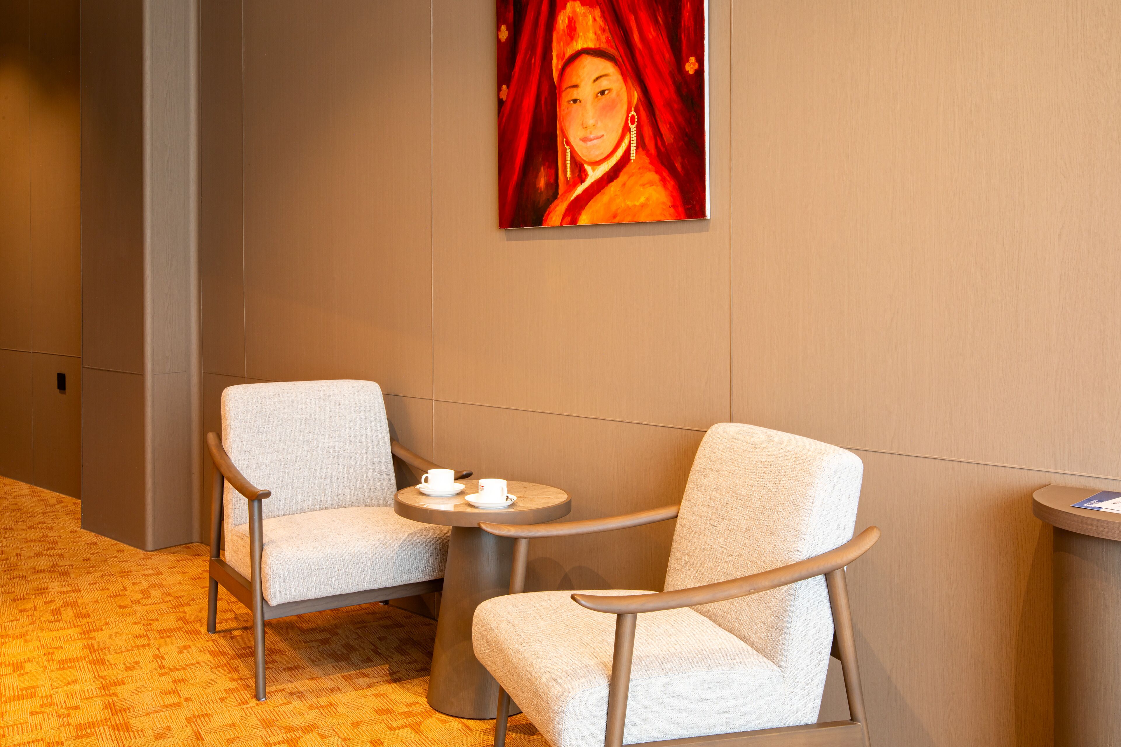 Un vestíbulo de hotel con dos sillones, una mesita con tazas y un cuadro en la pared.