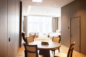 Habitación de hotel con una mesa redonda de comedor, sillas, una cama, un sofá y un ventanal con cortinas.