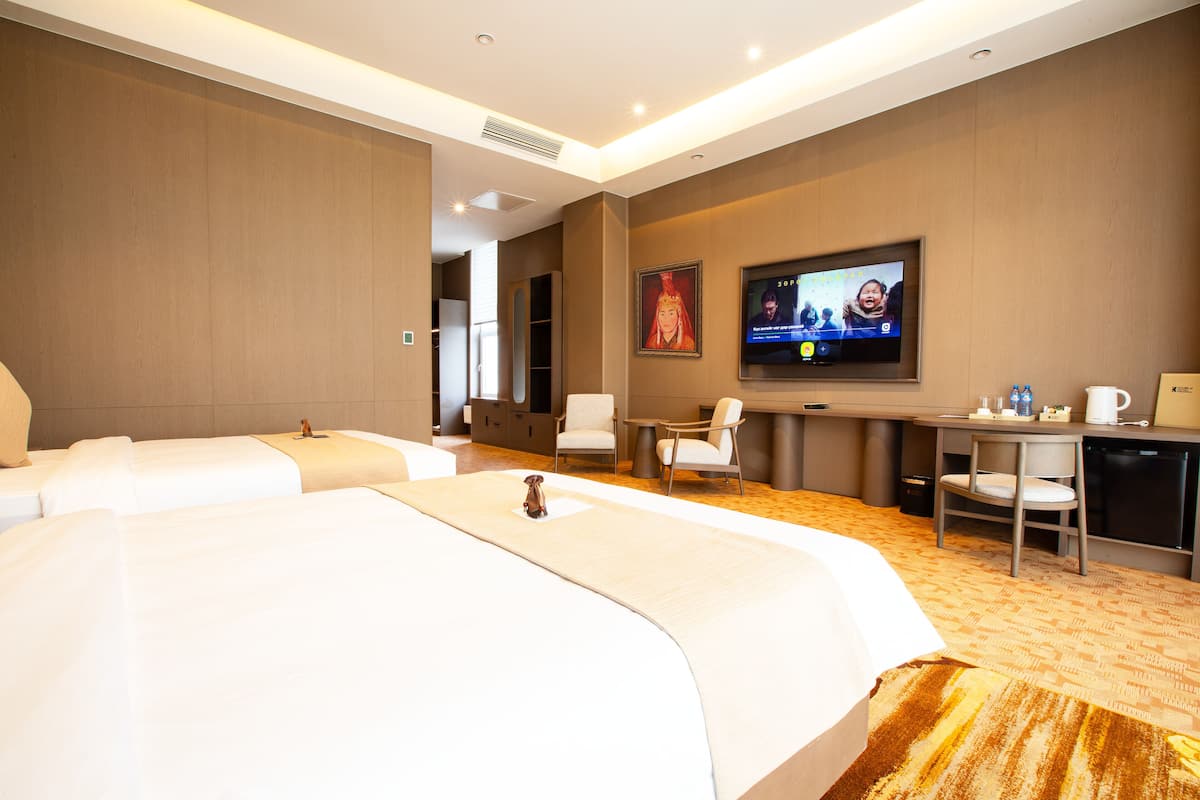 A hotel room with two beds, a desk, a chair, a television, and a coffee maker.