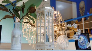 A decorative shelf with a white vase, a white lantern, and a clear glass vase with flowers. - Sheva Om (Pak Kret)