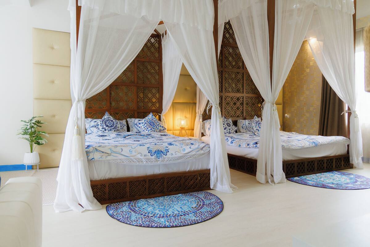 Una cama con dosel y cuatro columnas, con una colcha estampada, una planta en maceta y una alfombra decorativa.