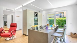 A modern kitchen with a central island, bar stools, and a red chair. - Casa Rudolfo Apartment With Private Garden (Riva del Garda)