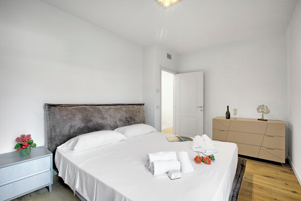 A neatly arranged bedroom with a large bed, a bedside table with a plant, a dresser, and a door leading to another room. - Casa Rudolfo Apartment With Private Garden (Riva del Garda)