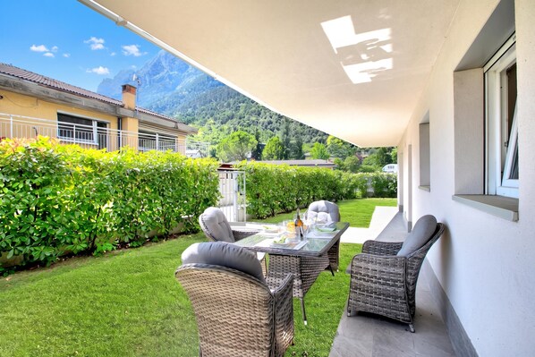 Une terrasse extérieure aménagée avec des meubles en osier, une table dressée pour le repas et une vue sur un paysage montagneux.