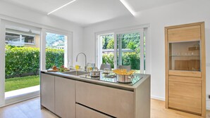 A modern kitchen with a large island, a built-in oven, and a glass-fronted cabinet. - Casa Rudolfo Apartment With Private Garden (Riva del Garda)