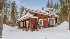 Puinen mökki, jossa on kuisti, ja jonka ympärillä on lumipeitteinen maa ja puita.