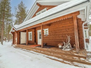 Eine Holzhütte mit überdachter Veranda, einer Eingangstür und einem kleinen Vorbereich mit Besen und Blumentöpfen.