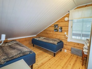 Ein kleiner, gemütlicher Raum mit zwei Betten, Holzwänden, einer schrägen Decke und einem Fenster mit Jalousien.