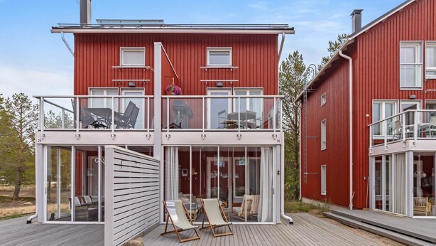 A modern red two-story house with a balcony, glass doors, and a wooden deck.