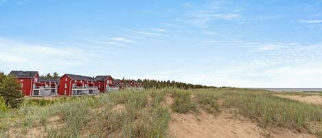 A row of red buildings with a sandy landscape and dunes in the foreground.