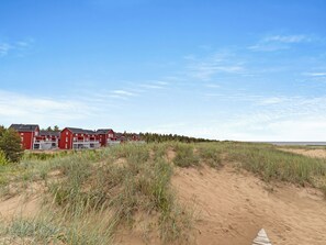 Eine Reihe roter Gebäude vor einer sandigen Landschaft mit Dünen im Vordergrund.