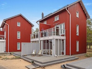 Una casa roja de dos pisos con un balcón, una terraza y un patio cercado.