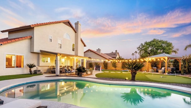 Una casa moderna con piscina, mobiliario exterior e iluminación con luces colgantes.