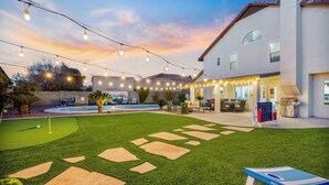 Un patio trasero con piscina, luces colgantes y zona de estar.