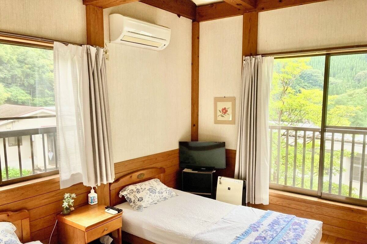 Una habitación pequeña y acogedora con una cama, un escritorio, un televisor y una ventana con vistas al verdor.