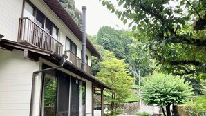 A traditional Japanese house with a wooden balcony, a gravel driveway, and lush greenery in the background. - INN KINOSATO (Morotsuka)