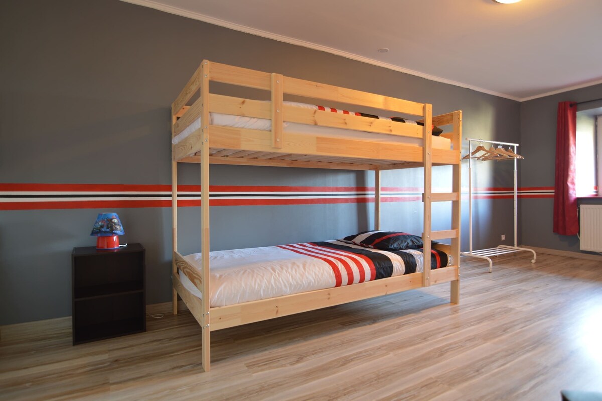 Un lit superposé avec une structure en bois, une petite étagère avec une lampe et un porte-manteau.