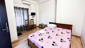 A bedroom with a bed, two chairs, a small table, a TV, and an air conditioning unit. - Assam Inn Grand  (Guwahati)