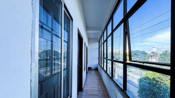 A corridor with large windows on both sides, leading to a door. - Assam Inn Grand  (Guwahati)