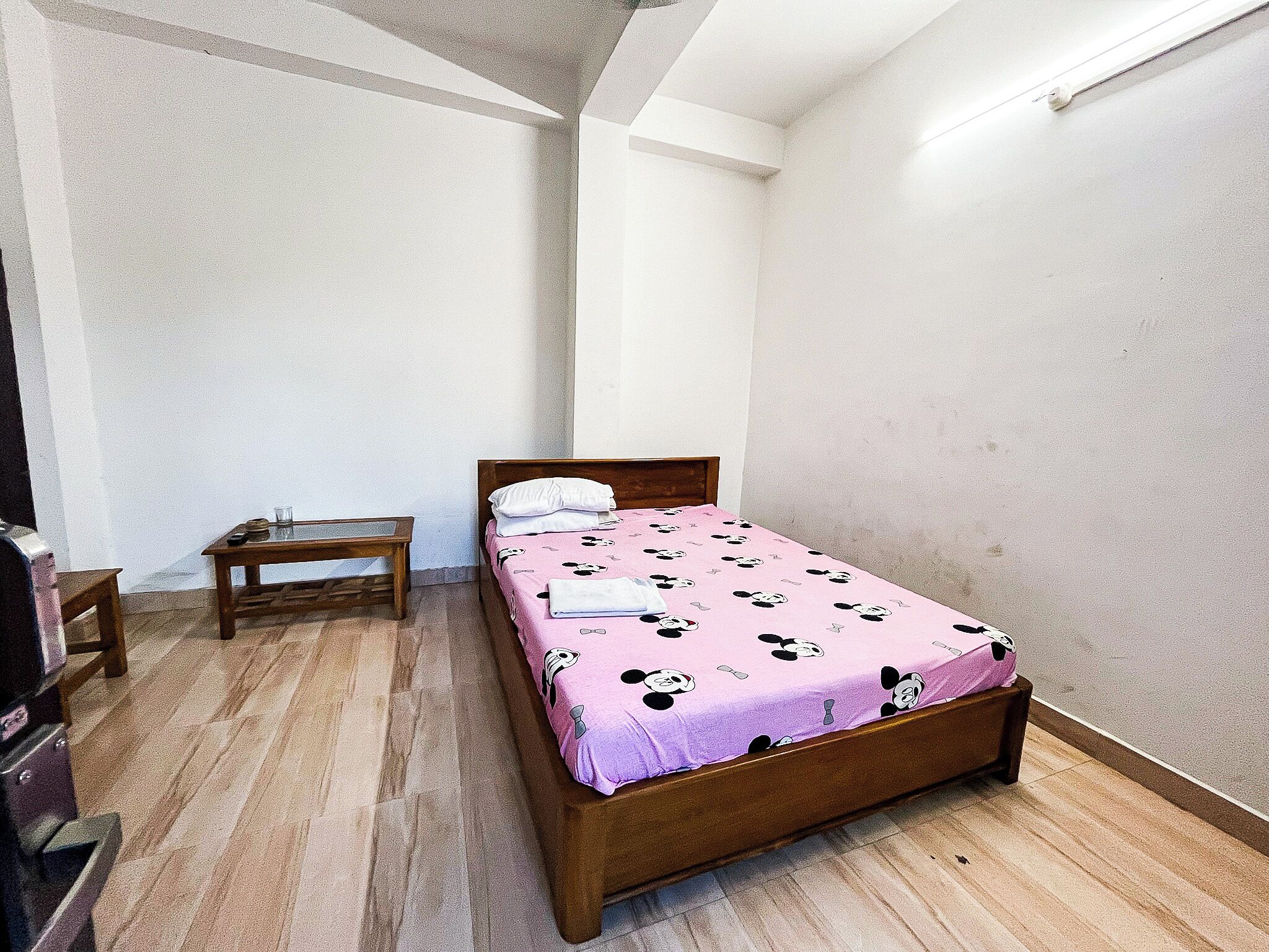 A small, neatly arranged bedroom with a single bed, a wooden nightstand, and a small table.