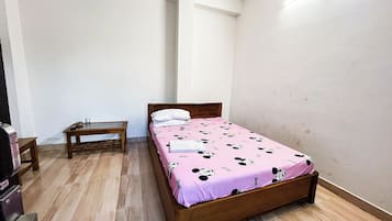 A small, neatly arranged bedroom with a single bed, a wooden nightstand, and a small table.