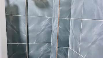 A shower with a handheld showerhead and a wall-mounted faucet. The shower area has dark blue tiles with visible grout lines.