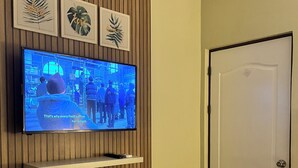 Une chambre d’hôtel avec un téléviseur fixé sur un mur recouvert de panneaux en bois, une porte blanche et un lit avec une literie blanche.