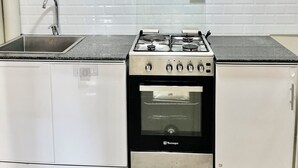 Une cuisine équipée d’une cuisinière à gaz, d’un four, d’un évier et de meubles blancs.
