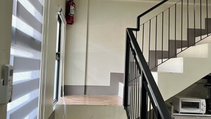 Un escalier avec une rampe noire, un extincteur fixé au mur et un grille-pain blanc posé sur un comptoir.
