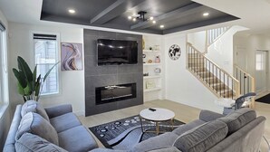 Una sala de estar moderna con un sofá seccional gris, un televisor de pantalla plana y una escalera que sube a otro nivel.