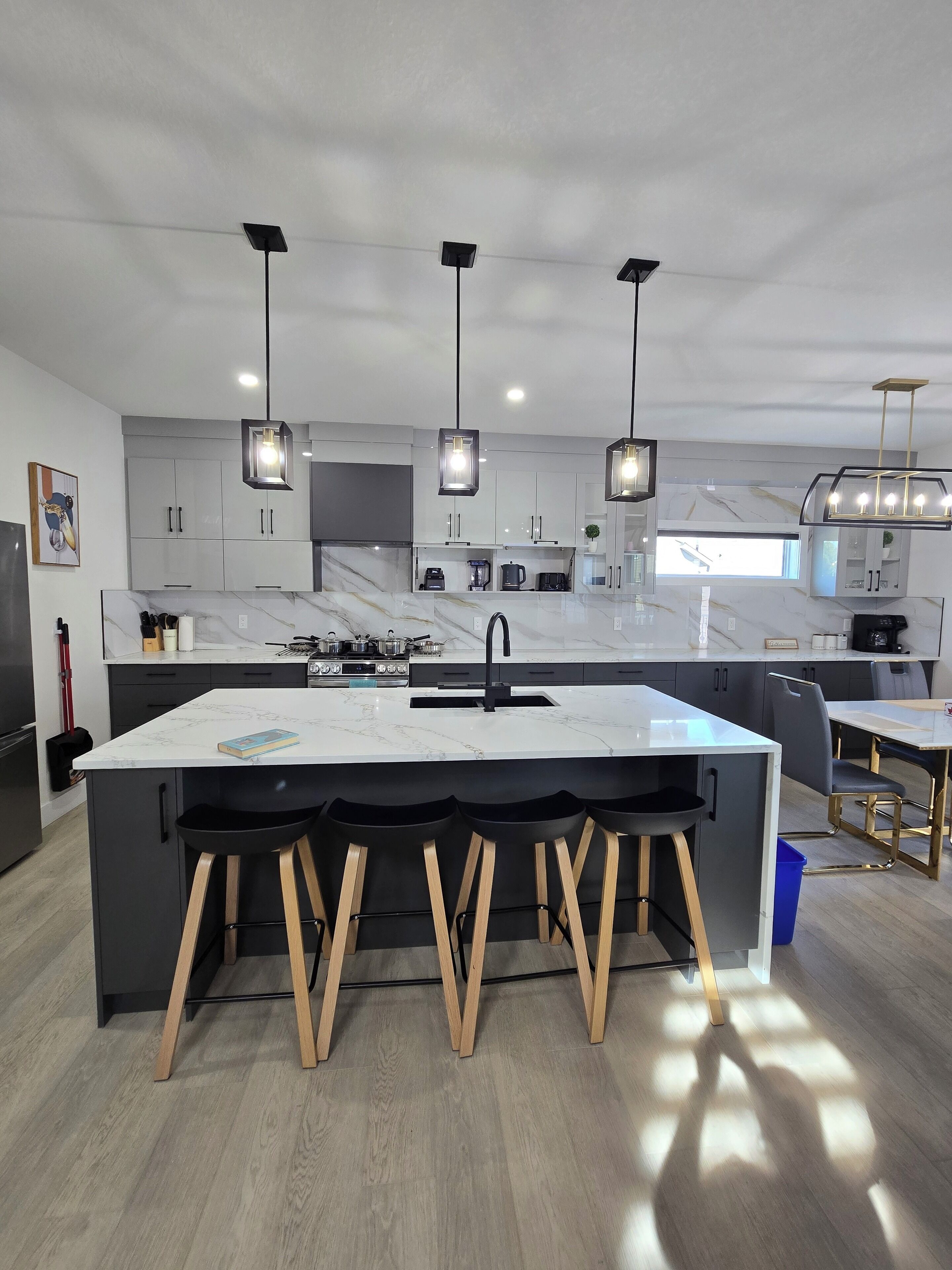 Une cuisine moderne dotée d’un grand îlot central, de tabourets de bar, de luminaires suspendus et offrant une vue sur l’extérieur.