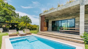 Una casa moderna con piscina, mobiliario exterior y un gran ventanal con vistas al jardín.