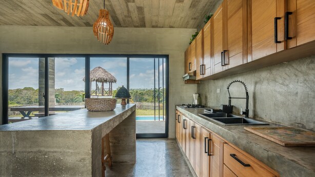 Una cocina moderna con armarios de madera, una isla grande y vistas a una construcción con techo de paja.