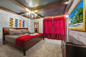 Une chambre avec un lit en bois, un rideau rouge, un tableau représentant une plage et un mur de briques orné de drapeaux.