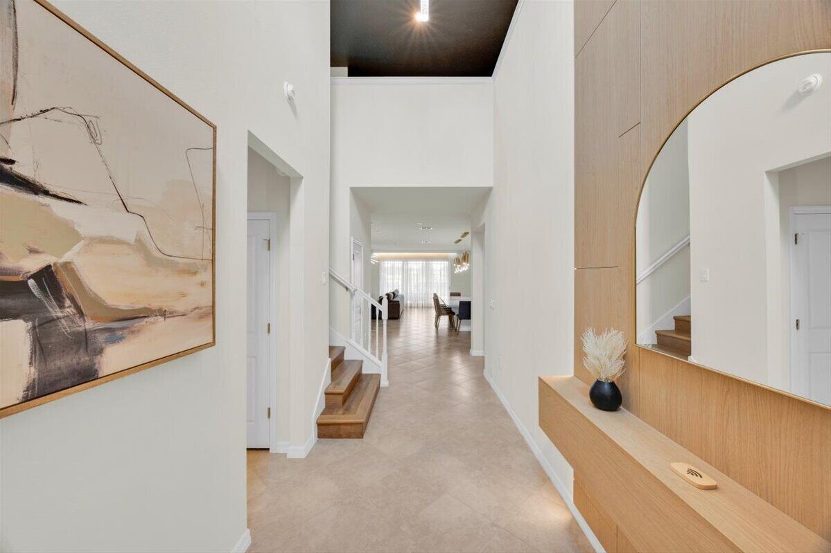 Un hall d’entrée spacieux avec un escalier menant à un deuxième étage, un grand miroir et une œuvre d’art moderne accrochée au mur.
