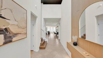 Un hall d’entrée spacieux avec un escalier menant à un deuxième étage, un grand miroir et une œuvre d’art moderne accrochée au mur.