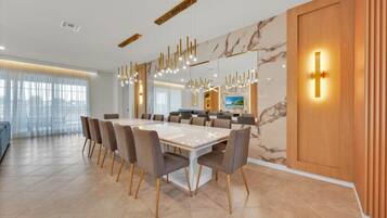 Un espace de restauration moderne avec un mur en marbre, une longue table entourée de chaises et des luminaires suspendus.