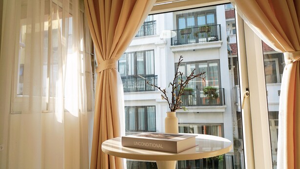Une pièce avec une fenêtre, des rideaux, un vase avec des branches et un livre intitulé « INCONDITIONNEL » posé sur une table ronde.