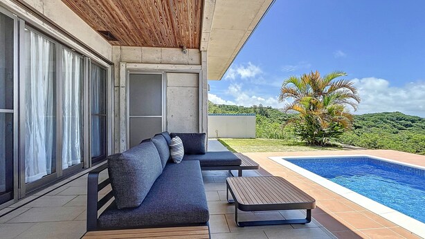 Un espacio al aire libre moderno con piscina, techo de madera y vistas a un paisaje exuberante.