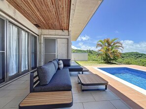 A modern outdoor seating area with a pool, a wooden ceiling, and a view of a lush landscape. - ulu Okinawa Resort (Motobu)