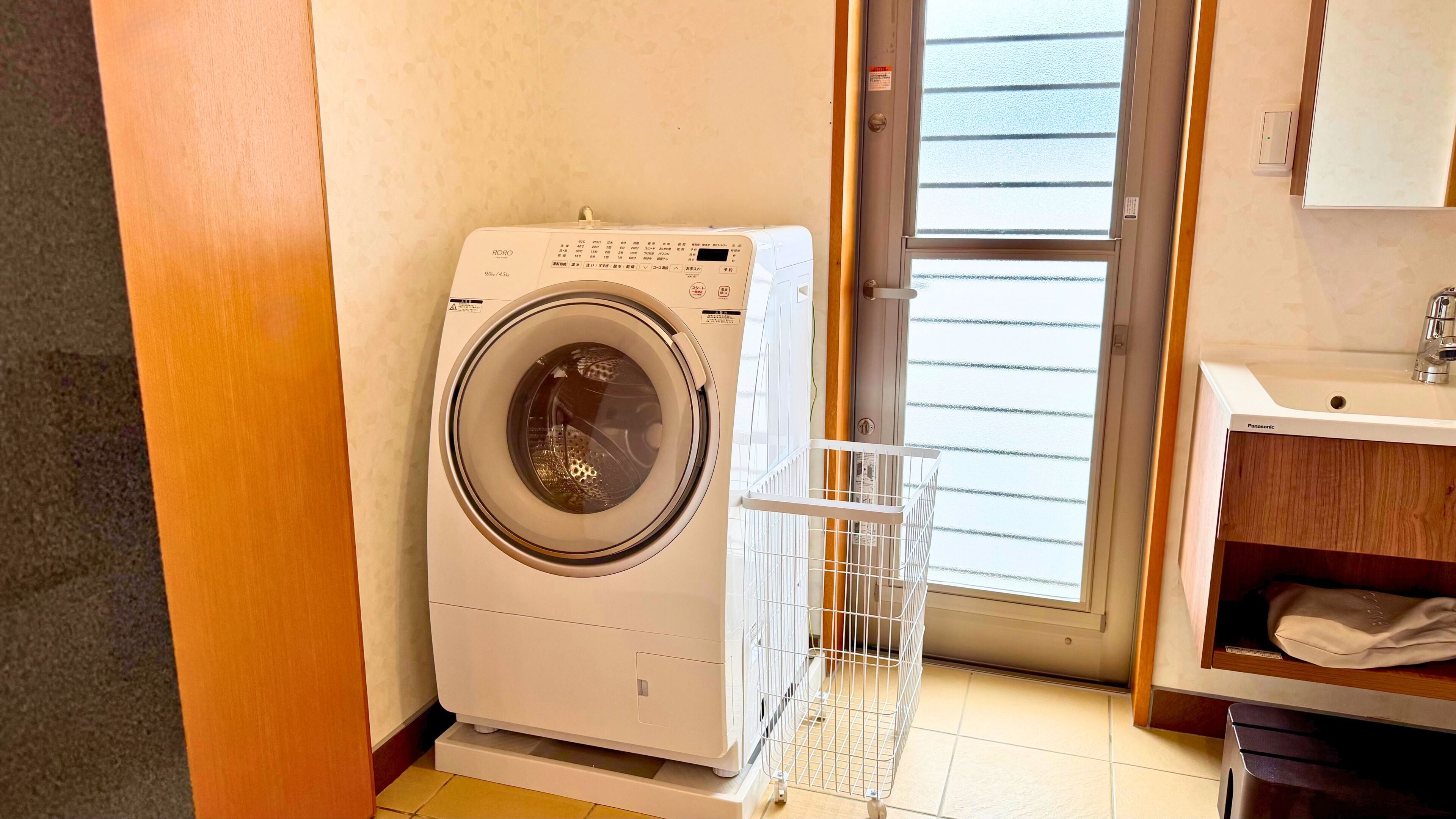 Una lavanderia compatta e moderna, con una lavatrice a carica frontale, un'asta appendiabiti in metallo e un bagno con lavandino e specchio.