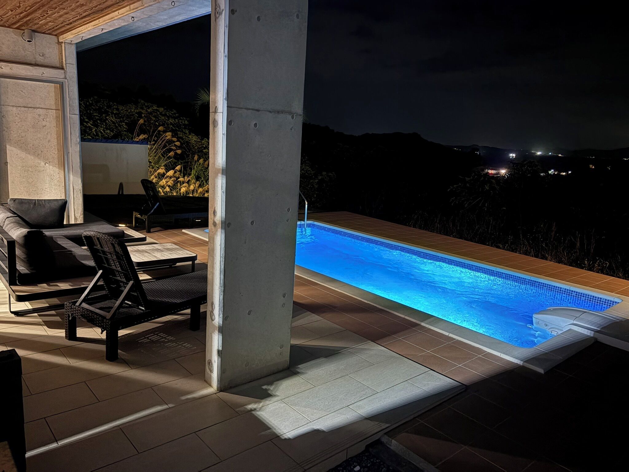 An outdoor pool area with a hot tub, lounge chairs, and a concrete pillar.