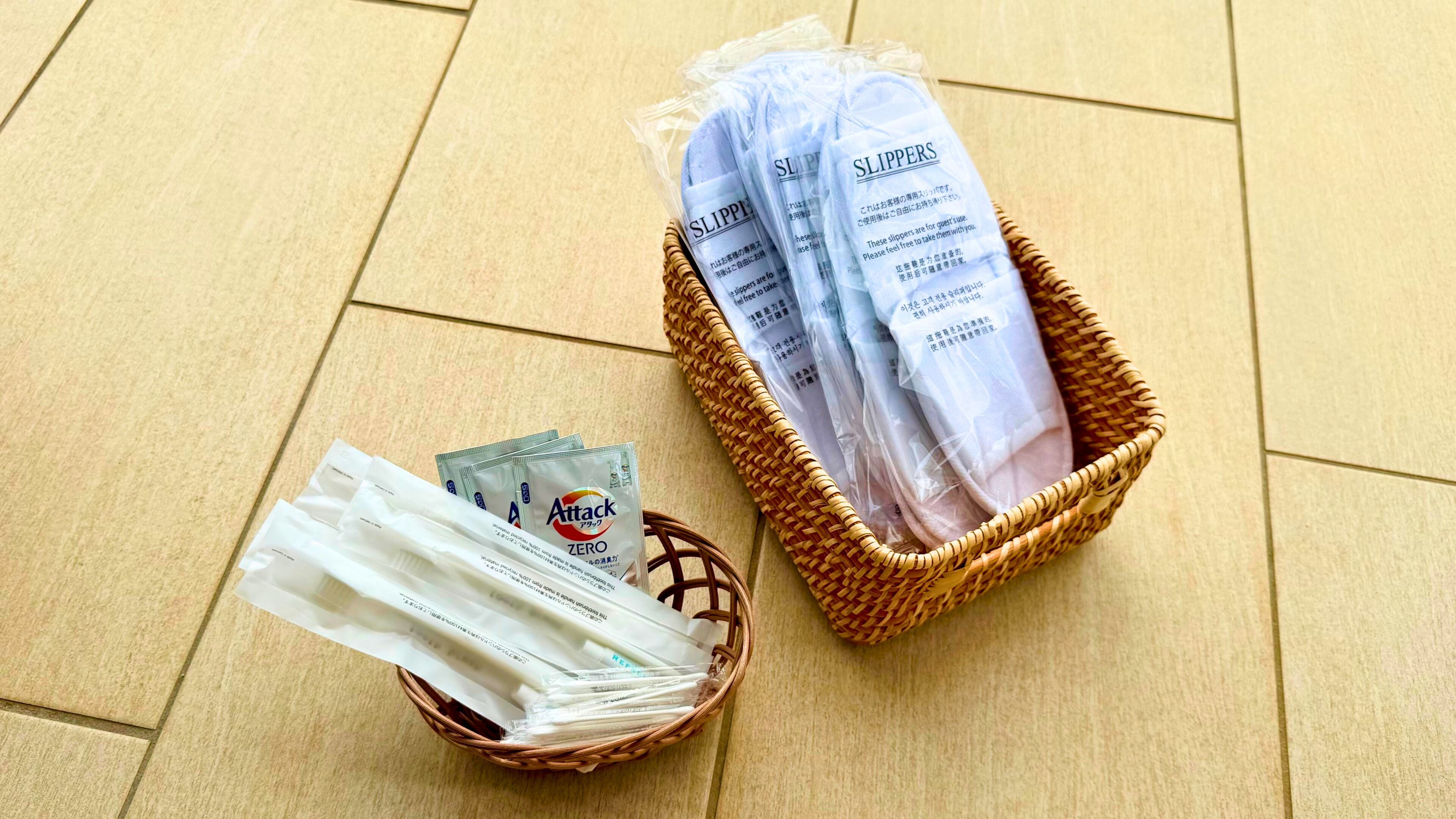 Uma cesta de vime com chinelos e uma cesta menor com pacotes de lenços.