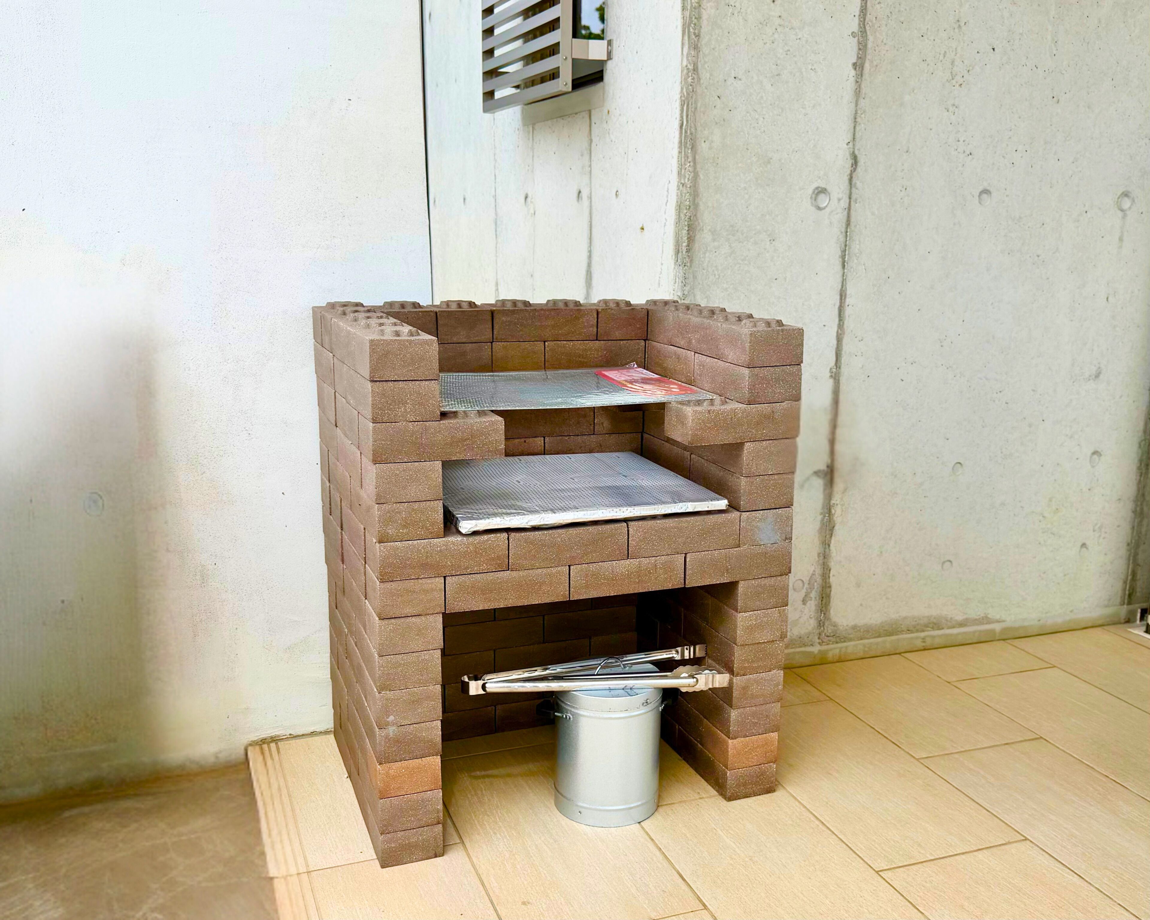 A brick-built barbecue grill with a metal shelf and a metal bucket underneath.